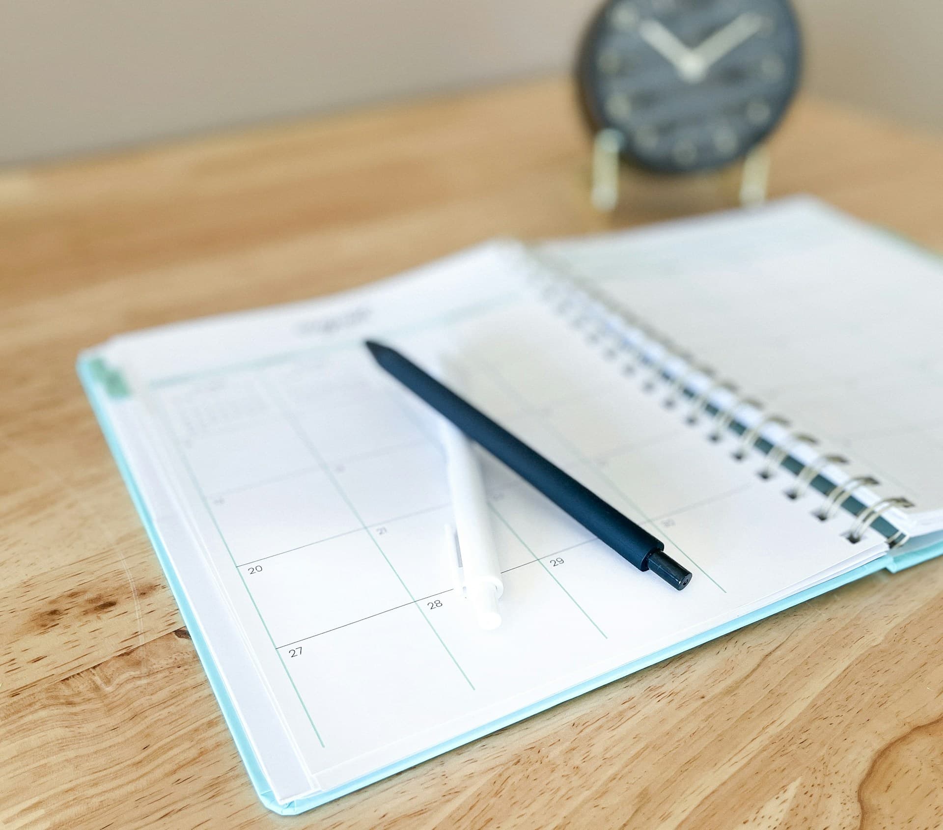 An open planner with a pen on a wooden desk
